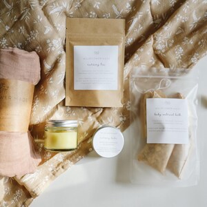 Peut inclure: Un coffret cadeau comprenant un tissu rose poudr&eacute; avec une bande en papier, un petit pot en verre de baume jaune, une bo&icirc;te ronde de pommade, un sachet en papier brun &eacute;tiquet&eacute; nursing tea et un sac transparent de sachets de bain &agrave; l'avoine.