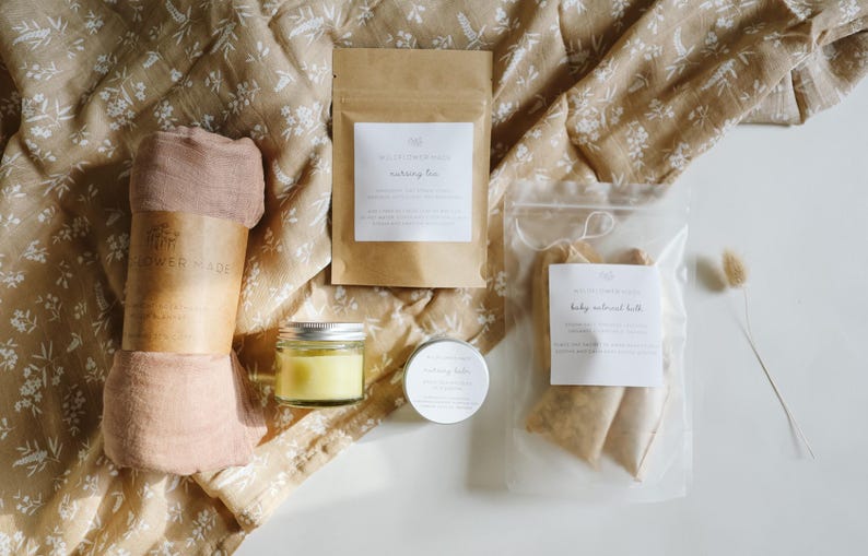 Peut inclure: Un coffret cadeau comprenant un tissu rose poudr&eacute; avec une bande en papier, un petit pot en verre de baume jaune, une bo&icirc;te ronde de pommade, un sachet en papier brun &eacute;tiquet&eacute; nursing tea et un sac transparent de sachets de bain &agrave; l'avoine.