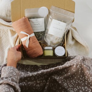 Peut inclure: Une bo&icirc;te cadeau en carton contenant un tissu en mousseline couleur terre cuite nou&eacute; avec un ruban blanc, un sachet de tisane d'allaitement, un sachet de sel de bain apaisant pour b&eacute;b&eacute;, un petit pot en verre et une petite bo&icirc;te ronde.