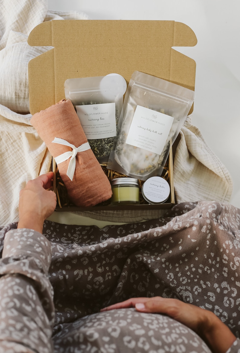 Peut inclure: Une bo&icirc;te cadeau en carton contenant un tissu en mousseline couleur terre cuite nou&eacute; avec un ruban blanc, un sachet de tisane d'allaitement, un sachet de sel de bain apaisant pour b&eacute;b&eacute;, un petit pot en verre et une petite bo&icirc;te ronde.