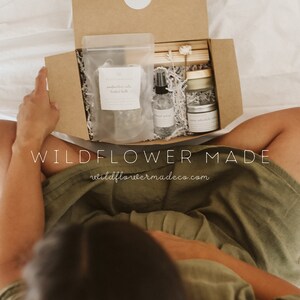 May include: A brown cardboard gift box containing a clear pouch of herbal bath, a small spray bottle, a jar with a gold lid, and wooden sticks. The box lid features a white circular sticker with the text Wildflower Made and the website address.