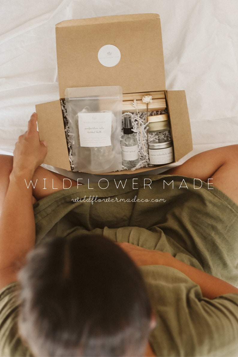 May include: A brown cardboard gift box containing a clear pouch of herbal bath, a small spray bottle, a jar with a gold lid, and wooden sticks. The box lid features a white circular sticker with the text Wildflower Made and the website address.