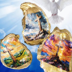 May include: Three oyster shells with gold-painted edges, each featuring a painted cross on a hill. The paintings depict a cross on a hill with colorful skies. A white dove is flying in the background against a blue sky.