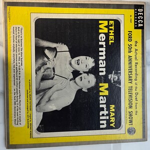 May include: A yellow and black record album cover featuring a black and white photo of Ethel Merman and Mary Martin. The album cover text reads "The Actual Recording of the Duet from the Ford 50th Anniversary Television Show!" and "Ethel Merman Mary Martin".