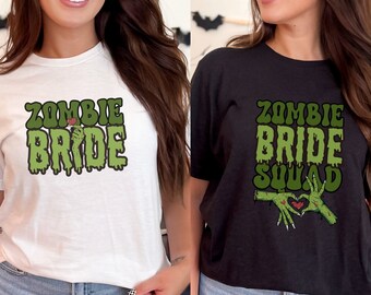 May include: Two t-shirts, one white and one dark gray, featuring a green and black graphic. The white shirt says "ZOMBIE BRIDE" with a zombie hand holding a red heart. The dark gray shirt says "ZOMBIE BRIDE SQUAD" with zombie hands forming a heart.