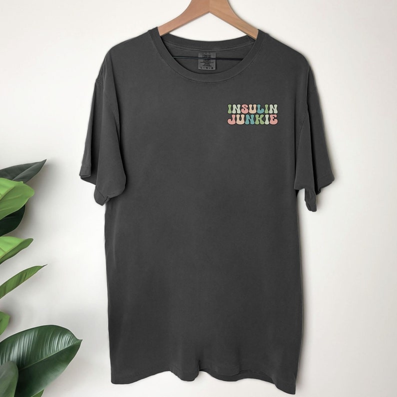 Może przedstawiać: Szary t-shirt z napisem "INSULIN JUNKIE" w kolorach tęczy z przodu.