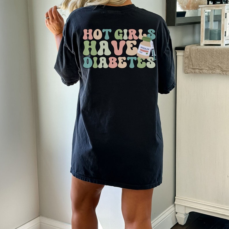 Może przedstawiać: Czarny, oversize'owy T-shirt z napisem "HOT GIRLS HAVE DIABETES" w kolorowej, retro czcionce. Obok tekstu znajduje się mały rysunek animowany butelki z insuliną.