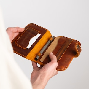 Peut inclure: Un carnet en cuir marron avec un porte-stylo et un emplacement pour carte. Le carnet est ouvert et l'intérieur est doublé de papier jaune.