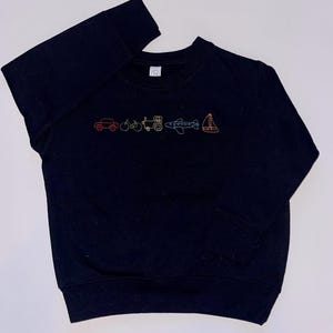 May include: Black long-sleeved sweatshirt with a colorful embroidered design of a car, bicycle, tractor, airplane, and sailboat.