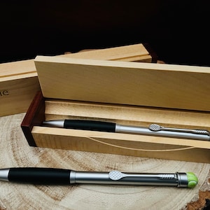 May include: Two silver pens with black barrels and green tennis ball accents are in a wooden box with the name "Eddie" engraved on the lid.