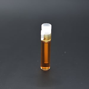 May include: A small, clear glass bottle with a white cap filled with a brown liquid. The bottle is standing on a black surface.