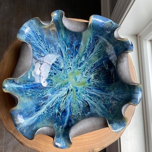 May include: A blue and green ceramic bowl with a wavy rim. The bowl has a speckled glaze with a white and yellow swirl in the center.