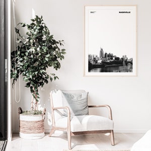 May include: Black and white photograph of the Nashville skyline with the text "NASHVILLE" in a white frame. The photograph is hanging on a white wall above a white armchair with a striped pillow.