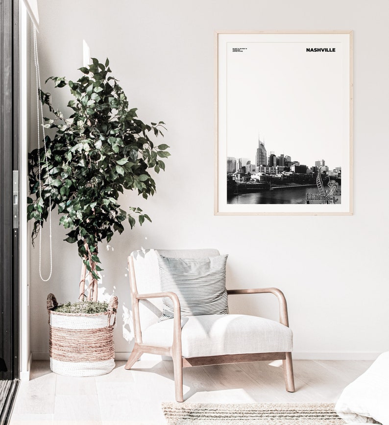 May include: Black and white photograph of the Nashville skyline with the text "NASHVILLE" in a white frame. The photograph is hanging on a white wall above a white armchair with a striped pillow.