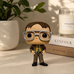 May include: A vinyl collectible figure featuring a character with brown hair, large silver-rimmed glasses, a yellow shirt, a green striped tie, and a brown suit. The figure stands with hands on hips, wearing black shoes, and has a tan complexion.