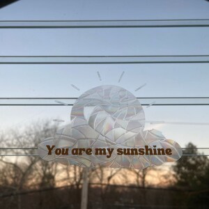 以下が含まれることがあります： 太陽と雲のデザインと「You are my sunshine」というテキストが書かれた透明なステッカーです。