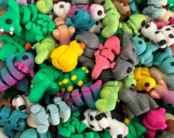 May include: A collection of colorful, small, 3D printed figurines. The figurines are in various shapes and sizes, including animals, plants, and abstract designs. The figurines are made of a smooth, plastic-like material.