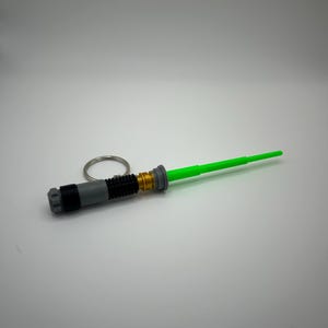 May include: A green lightsaber keyring with a silver and black handle and a gold accent.