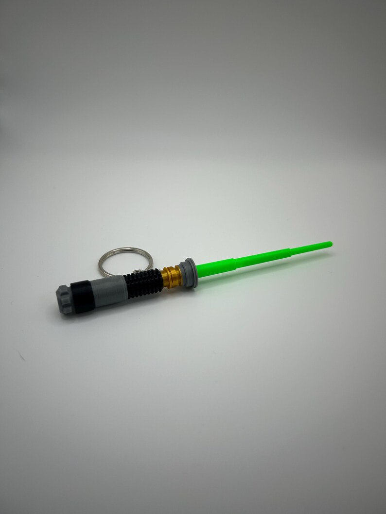 May include: A green lightsaber keyring with a silver and black handle and a gold accent.