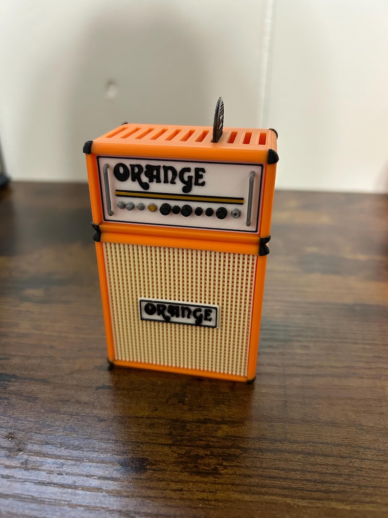 May include: Orange brand guitar amplifier with a black and orange colour scheme. The amplifier has a speaker grill and a control panel with knobs.