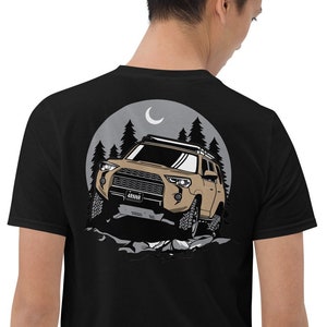 May include: Black t-shirt with a graphic of a brown SUV driving through a forest at night with a crescent moon in the sky.