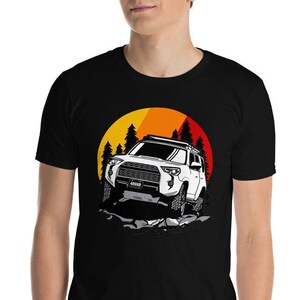 May include: Black t-shirt with a graphic of a white off-road vehicle set against a sunset and pine trees. The design showcases a 4x4 truck illustration, ideal for those who enjoy the outdoors.
