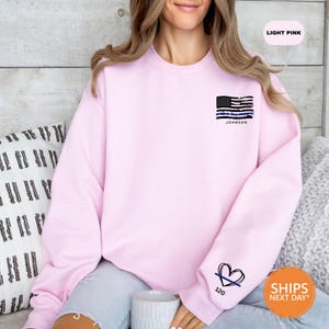 a woman sitting on a couch wearing a pink sweatshirt