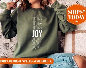 May include: A green sweatshirt with the words "JOY" and "LOVE" printed in white on the front. The sweatshirt is being modelled by a person wearing blue jeans.