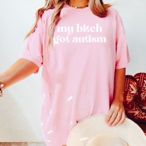 a woman wearing a pink shirt that says, my bitch got autism