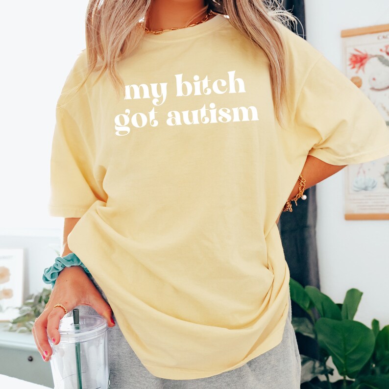 a woman wearing a yellow t - shirt that says, my bitch got autism