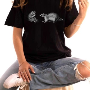 May include: A black t-shirt with a graphic print of two raccoons facing each other. The raccoons are drawn in a vintage style.