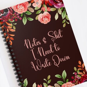 May include: A dark brown spiral notebook with a floral design and the text "Notes & Shit I Need to Write Down" in pink.