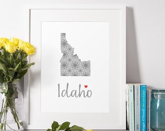 May include: A white framed print with a gray outline of the state of Idaho with a gray and white patterned design. The word "Idaho" is written in gray script with a small red heart next to it.