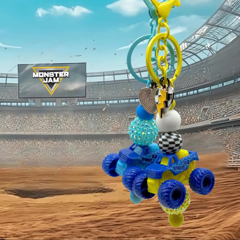 Pu&ograve; includere: Un portachiavi a forma di monster truck blu e giallo con una variet&agrave; di perline e ciondoli decorativi. Il portachiavi include un ciondolo a forma di cuore, un ciondolo a scacchi e una combinazione di colori blu e giallo. Lo sfondo mostra uno stadio con il logo Monster Jam.