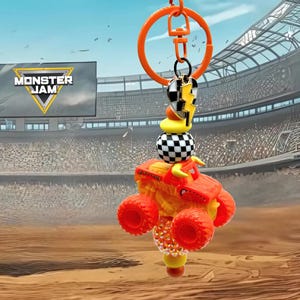 Pu&ograve; includere: Portachiavi arancione con un camion mostro in miniatura con ruote rosse e carrozzeria gialla e arancione. Il portachiavi include un ciondolo con un motivo a scacchi e la scritta "Monster Jam".