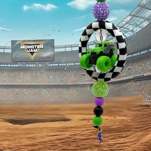 May include: A car charm with a green monster truck toy inside a black and white chequered ring. The charm has purple, green, and black beads, a purple pineapple bead, and a lightning bolt charm. The background shows a stadium with the "Monster Jam" logo.
