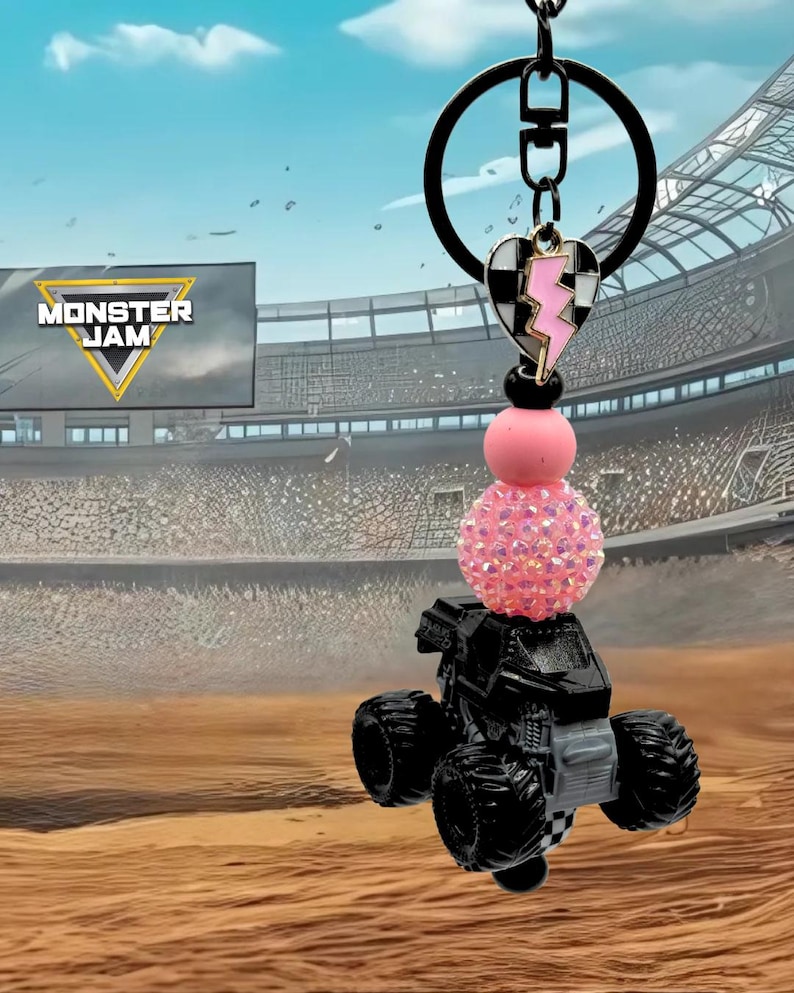 Pu&ograve; includere: Portachiavi nero con camion mostro con una perla rosa scintillante e un ciondolo a forma di cuore con un fulmine. Il portachiavi ha un anello nero e un logo Monster Jam sullo sfondo.