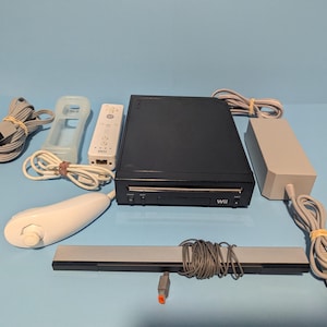 May include: A black Wii console with a matching remote, sensor bar, and power supply. The set includes a white remote, a clear protective sleeve, and various connecting cables. The console has a disc drive and the Wii logo.