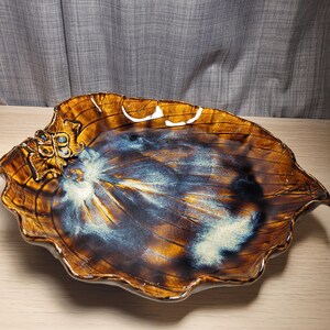 May include: A large, brown ceramic serving dish shaped like a leaf with a raised, textured design. The dish has a glossy finish with blue and white accents.
