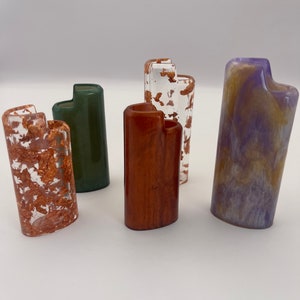 May include: Five rectangular lighter cases with rounded corners. One is clear with copper flakes, one is solid dark green, one is solid reddish-brown, one is clear with gold flakes, and one features a marbled blend of purple and gold resin.