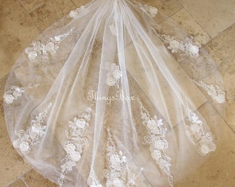 May include: A white bridal veil with floral lace appliques and delicate pearl accents. The veil is made of sheer fabric and features a comb for easy placement. The text "Things Box" is visible on the veil.