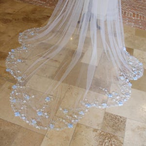 May include: A white bridal veil with a scalloped edge and delicate blue floral embroidery.