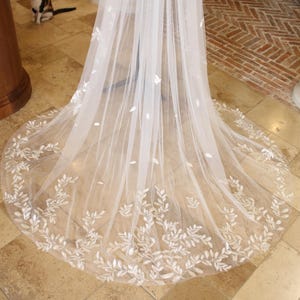 May include: White tulle wedding veil with a delicate floral design. The veil has a scalloped edge and is decorated with small, white leaves.