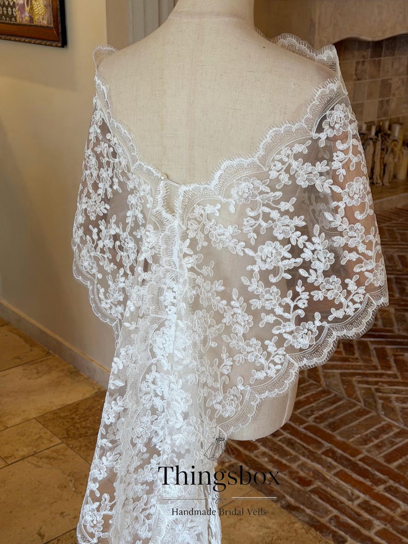 May include: A white lace bridal veil draped over a mannequin. The veil features a floral pattern and scalloped edges. The text "Thingsbox Handmade Bridal Veils" is visible at the bottom.