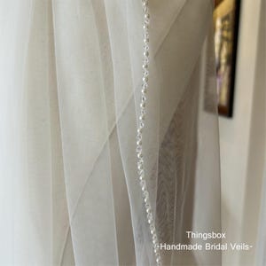 May include: A white bridal veil with a beaded trim. The veil is made of soft tulle and has a delicate, romantic look.