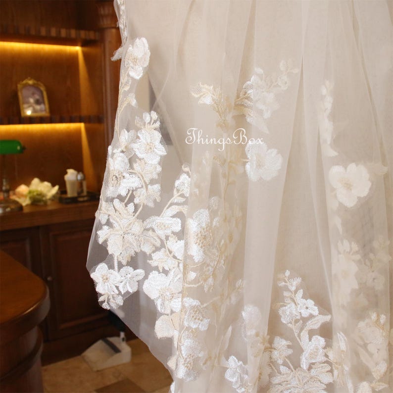 May include: A white bridal veil with delicate floral embroidery. The veil is made of soft tulle and features a delicate floral pattern.