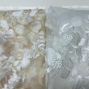 May include: Two swatches of tulle fabric with floral embroidery. The left swatch is champagne tulle with champagne lace. The right swatch is ivory tulle with white lace.