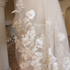May include: A delicate ivory bridal veil with floral embroidery. The veil is made of soft tulle and features a delicate floral pattern in a light gold color. The veil is perfect for a romantic wedding.