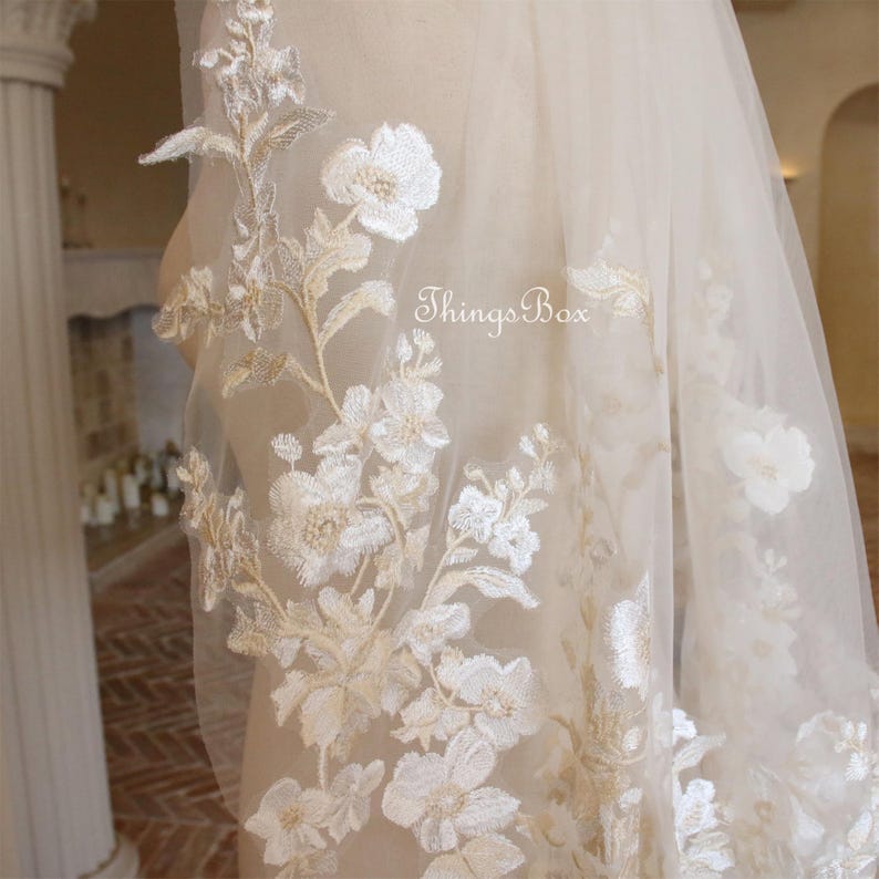 May include: A delicate ivory bridal veil with floral embroidery. The veil is made of soft tulle and features a delicate floral pattern in a light gold color. The veil is perfect for a romantic wedding.