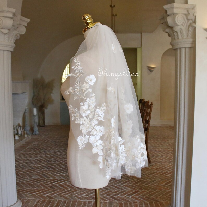 May include: A white bridal veil with delicate floral embroidery. The veil is made of soft tulle and features a scalloped edge.